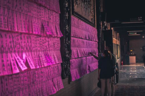 Free Individuals examine vibrant prayer cards in a serene Vietnamese temple, Ho Chi Minh City. Stock Photo