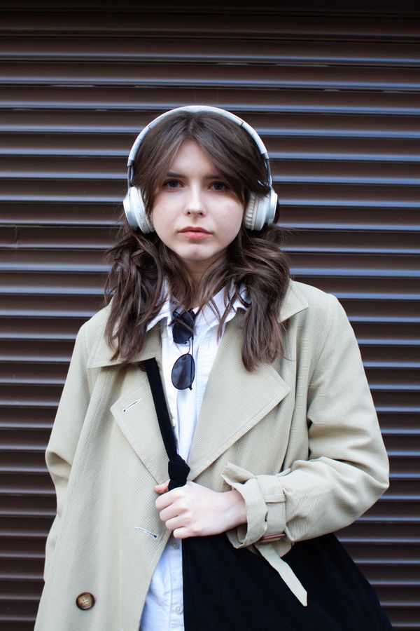 Woman in a trench coat wearing headphones outdoors — photo by Diana Onfilm on Pexels