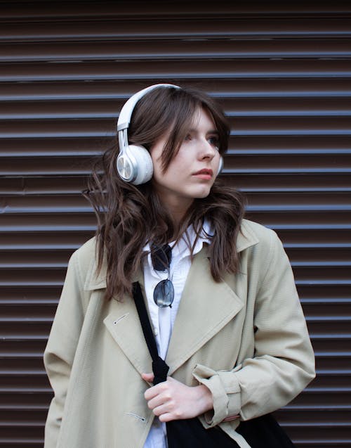 A Woman in Beige Coat Wearing Headphones while Looking Over Shoulder