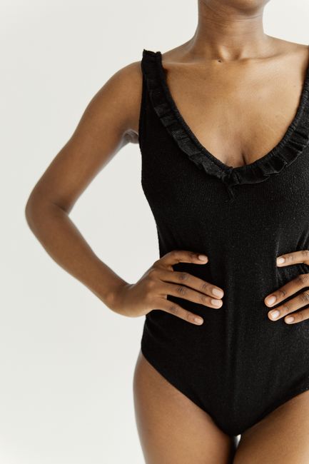 Stylish portrait of a woman in a sleek black bodysuit against a white background.