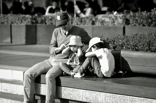 Free A father and children share a quiet moment on a park bench, captured in black and white. Stock Photo