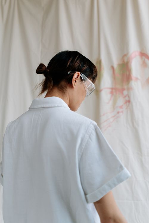 Free Back view of an artist wearing safety goggles and a white shirt, creating art indoors. Stock Photo
