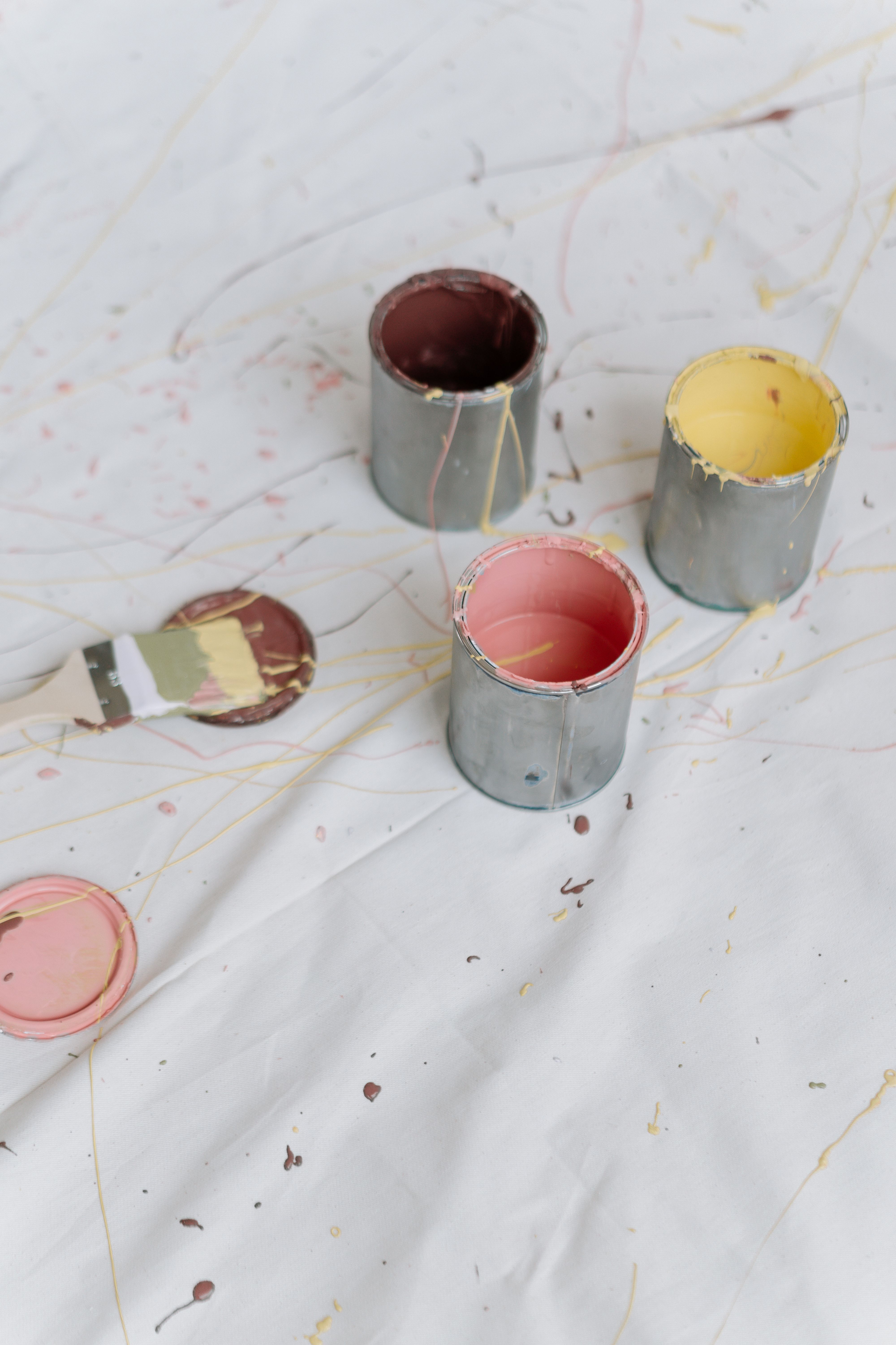 Three paint cans with brushes on a splattered canvas, showcasing vibrant hues.