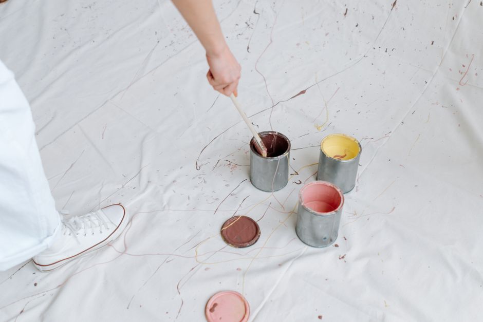 Close-up of paint cans and brushes on a white fabric backdrop, creating a messy artistic scene.