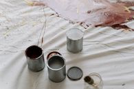 Three open paint cans on canvas with splattered paint, depicting an artistic setting.