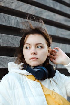 Portrait of a woman with black headphones and white jacket outdoors, looking over her shoulder.