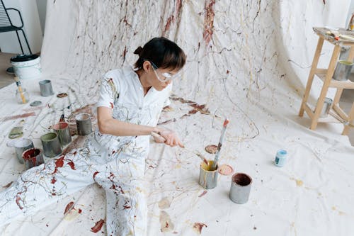 Woman in Paint Overalls Sitting on White Fabric with Splashes of Paint 