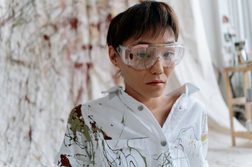 Free Portrait of an artist in a paint-splattered shirt and goggles, indoors in a studio setting. Stock Photo