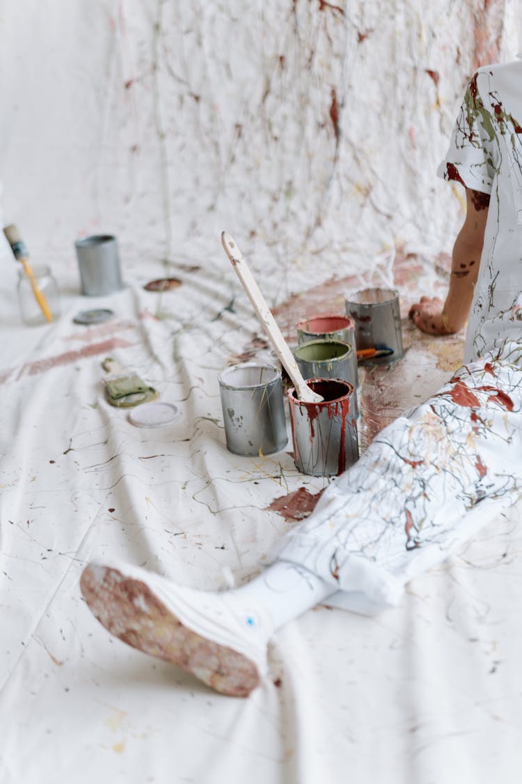 A Person With Pain On Clothes Sitting Beside Cans Of Paint