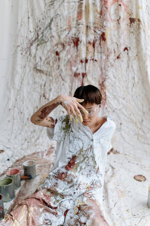 A Person with Paint on Clothes and Arm Sitting on White Textile