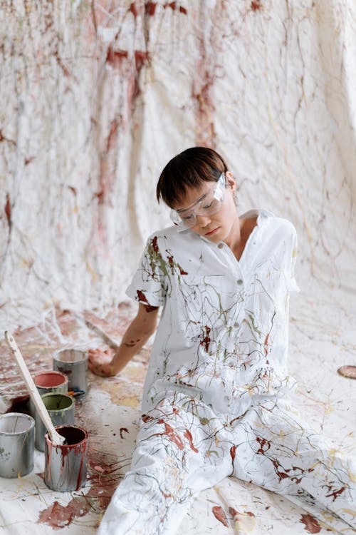 Woman in Paint Overalls Sitting on White Fabric with Splashes of Paint 