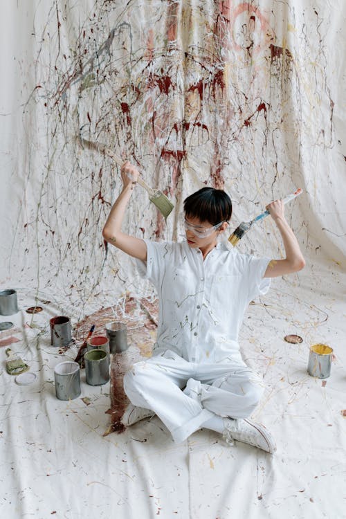 A Man in White Coveralls Holding Paint Brushes