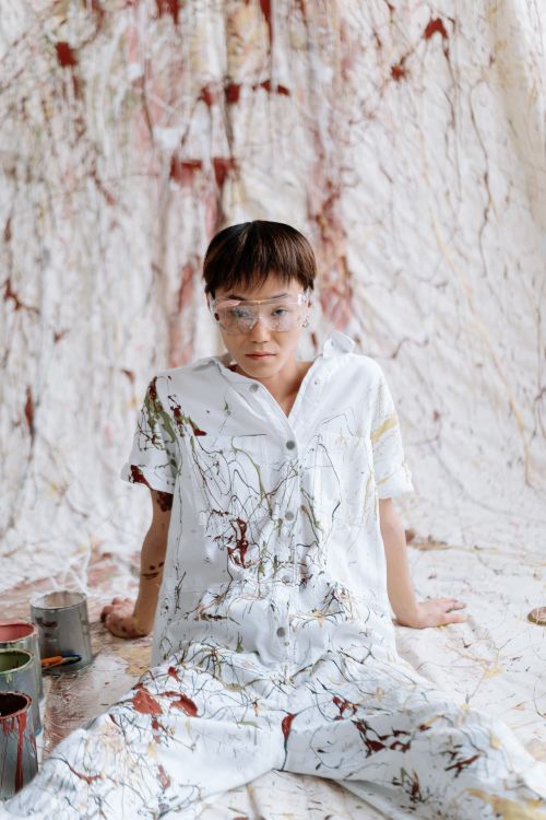 Free A person in paint-splattered coveralls sitting indoors, embodying creativity and artistic expression. Stock Photo