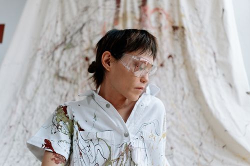 Free Artist in a splattered shirt wearing safety glasses, immersed in painting. Stock Photo