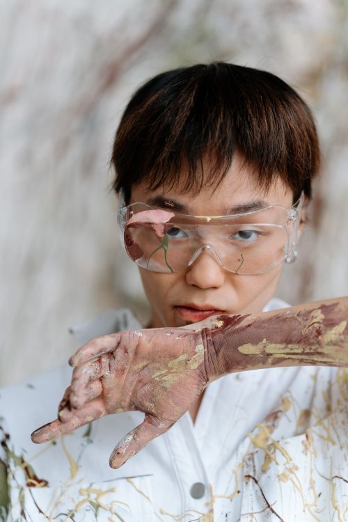 Free Portrait of an Asian artist with paint-covered hands and safety glasses, conveying creativity and protection. Stock Photo