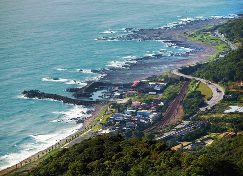 A stunning aerial shot of Taiwan's coastline, showcasing rocky shores, lush greenery, and a winding road along the ocean.