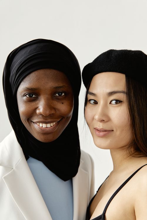 Free Portrait of two diverse women, one in hijab, smiling and embracing each other warmly. Stock Photo