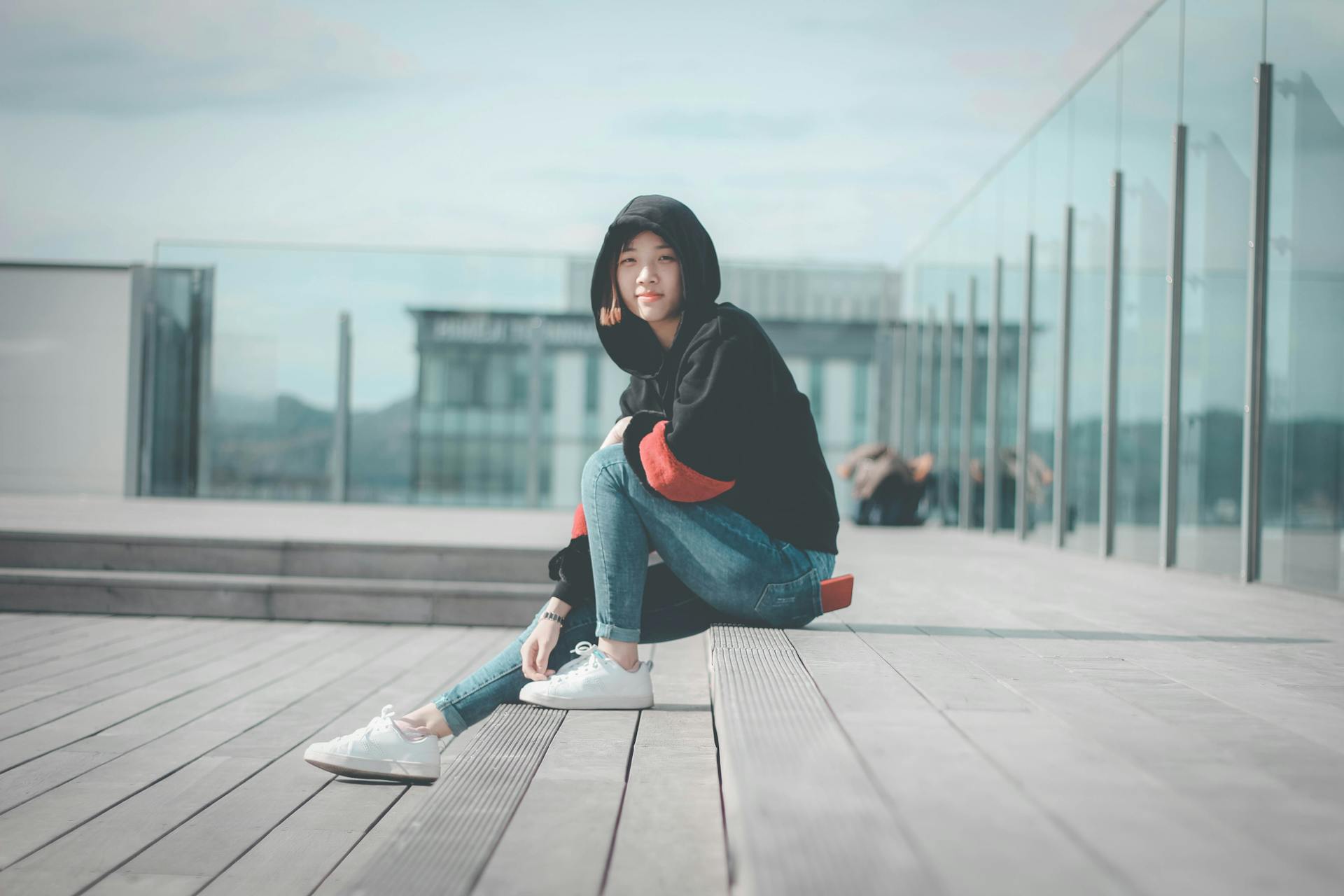 Stylish young woman sitting in an urban setting wearing a comfy hoodie and jeans.