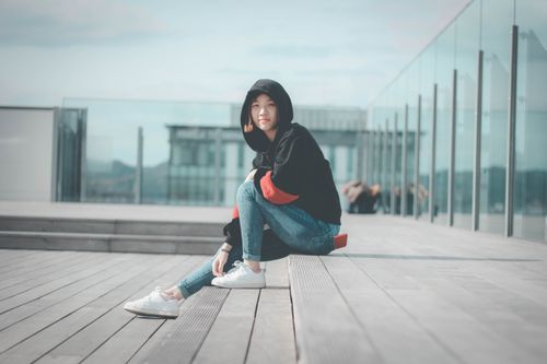 Free Stylish young woman sitting in an urban setting wearing a comfy hoodie and jeans. Stock Photo