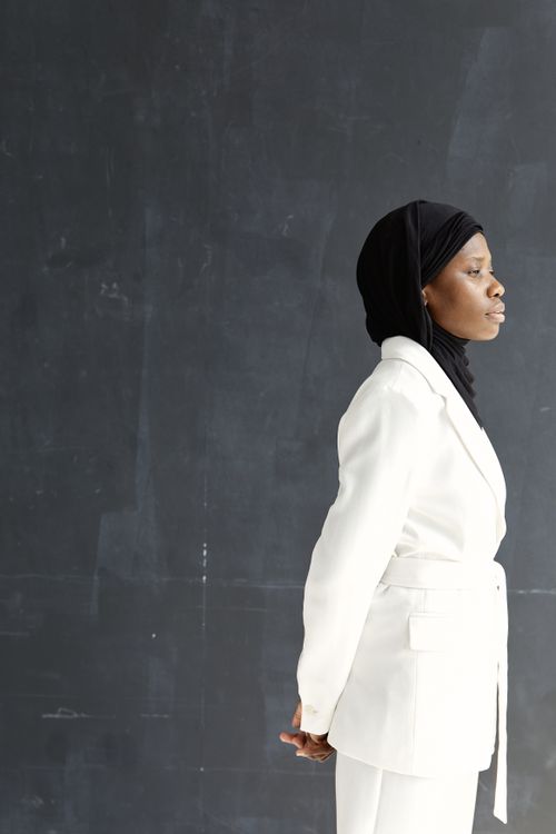 Free Stylish woman in a white suit and hijab posing side view against a dark background. Stock Photo
