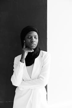 Black and white portrait of an African American woman in a hijab, wearing a white outfit, looking reflective.