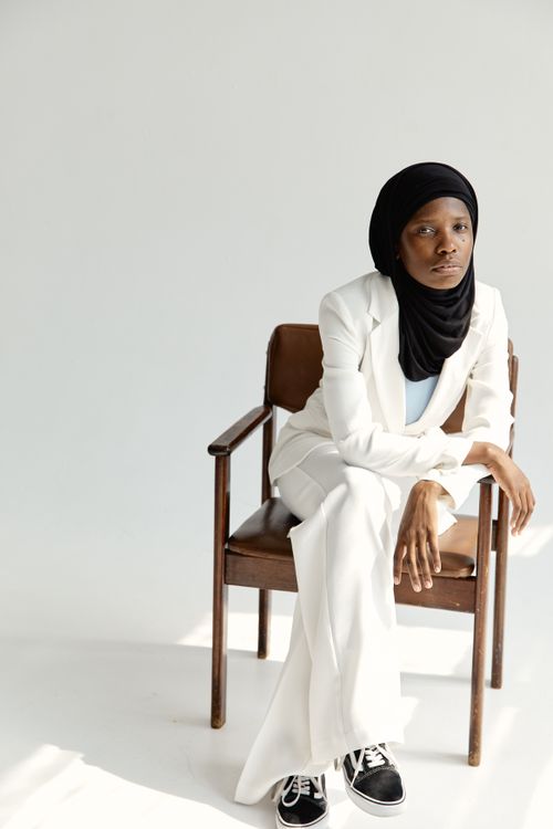Free Elegant African American woman wearing hijab and white suit sitting on wooden chair. Stock Photo