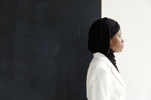 Free Side view of a woman in a hijab standing against a dark background, emphasizing contrast and simplicity. Stock Photo