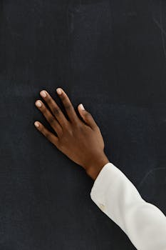Close-up of a hand on a dark chalkboard, creating a contrast in texture and color.
