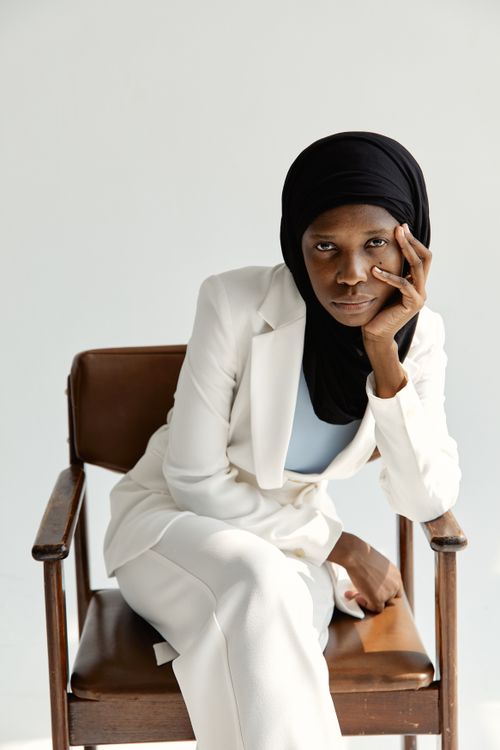 Free African American woman sitting on a chair in a white suit, wearing a hijab, with a thoughtful expression. Stock Photo