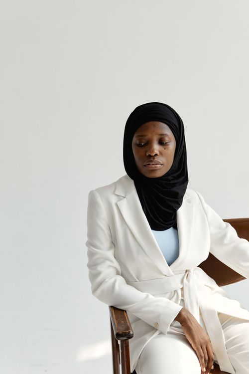 Free Portrait of an elegant woman wearing a white suit and hijab, seated indoors with soft lighting. Stock Photo