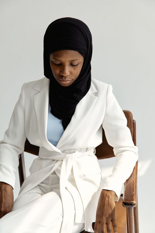 Free Studio portrait of a woman in a white suit and black hijab, seated against a white background. Stock Photo