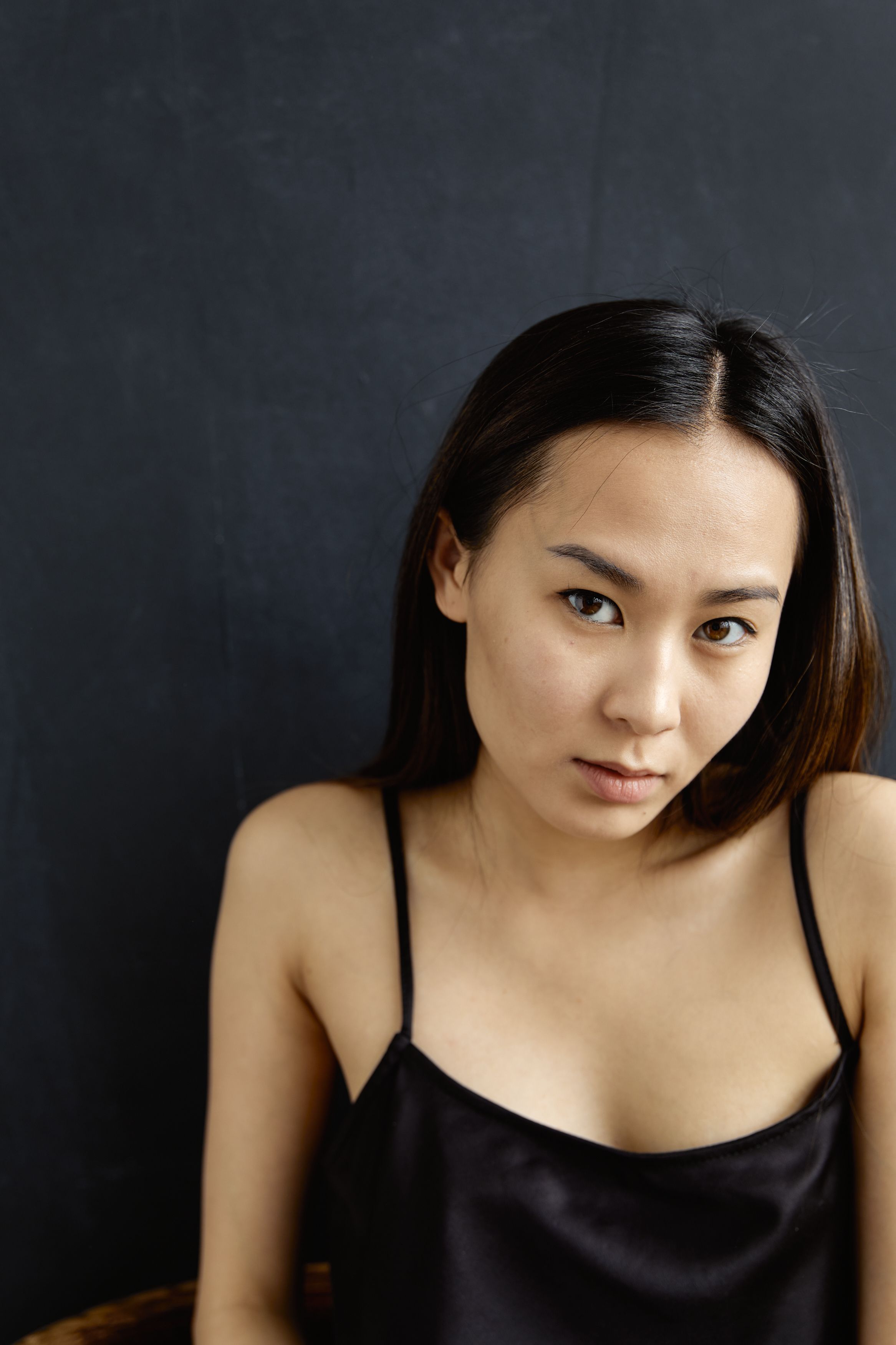 A striking portrait of a young woman in a black spaghetti strap top against a dark background.