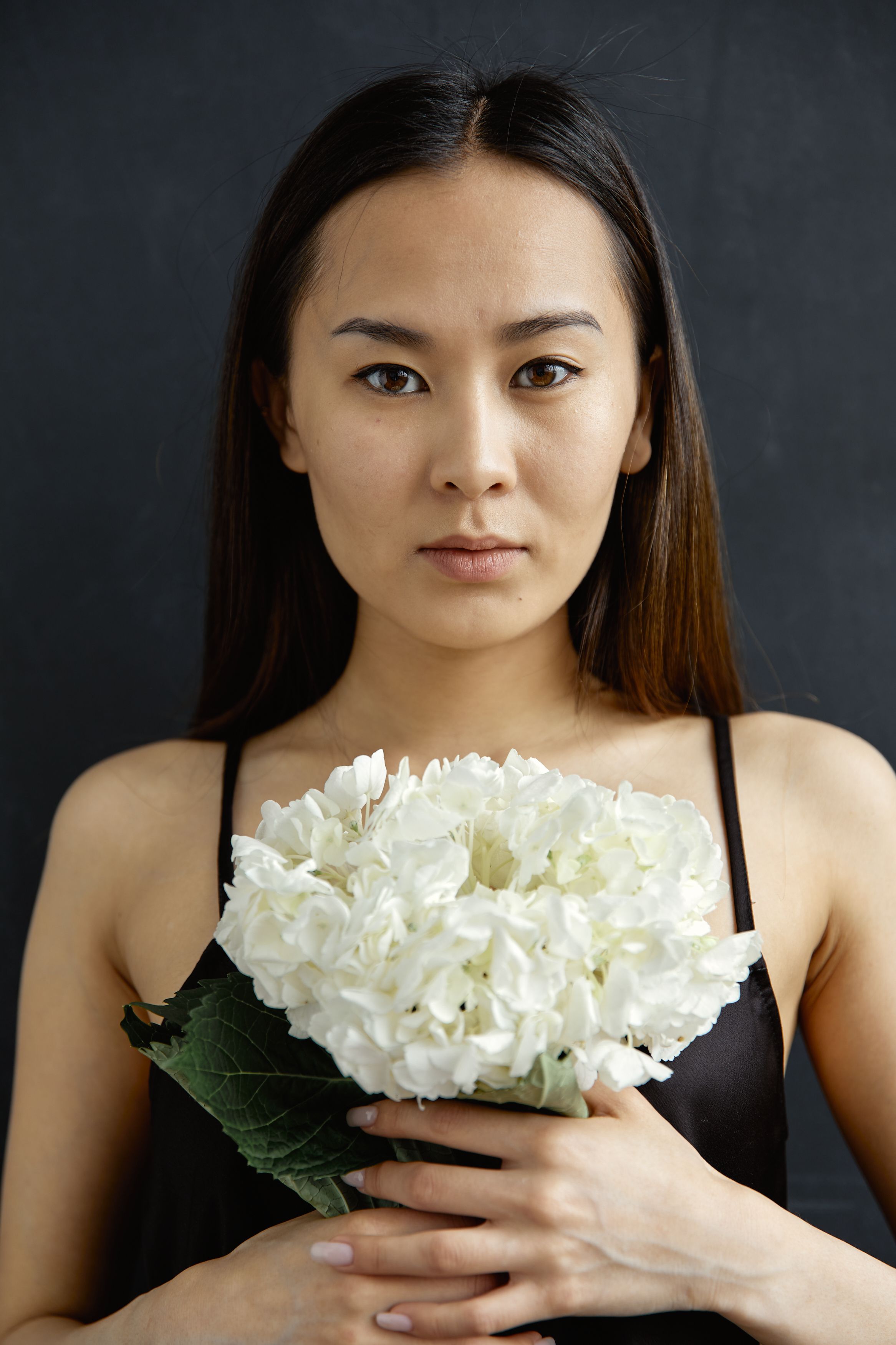 Asian woman holding a white flower bouquet against a dark studio background.