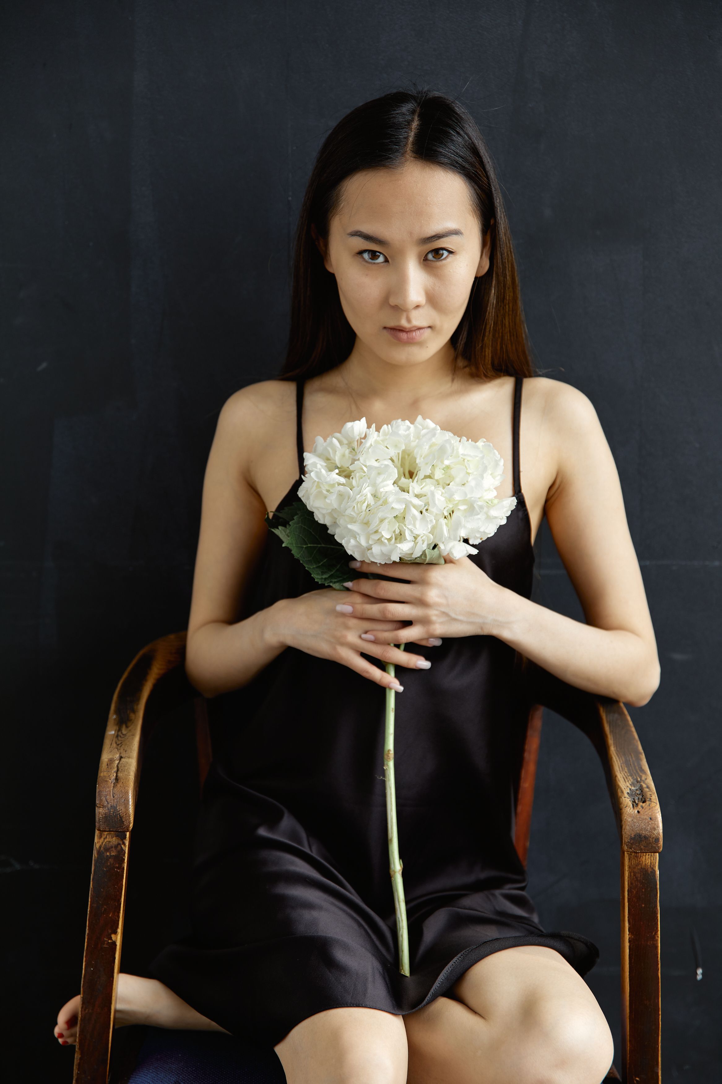 A serene portrait of a woman holding white flowers, seated against a dark background.