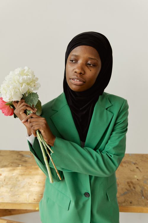 Free Stylish woman wearing hijab and green suit holding a bouquet of flowers in a studio setting. Stock Photo