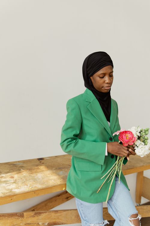 Free Portrait of a woman in a green blazer holding flowers, indoors, exuding elegance and style. Stock Photo
