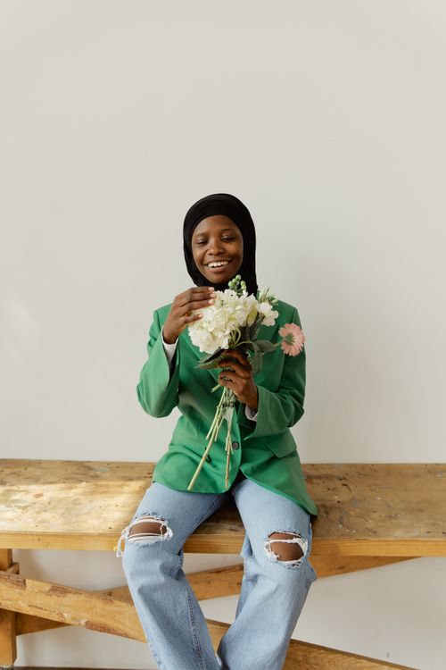 Free A smiling woman in a hijab holds a bouquet of flowers while sitting indoors. Stock Photo