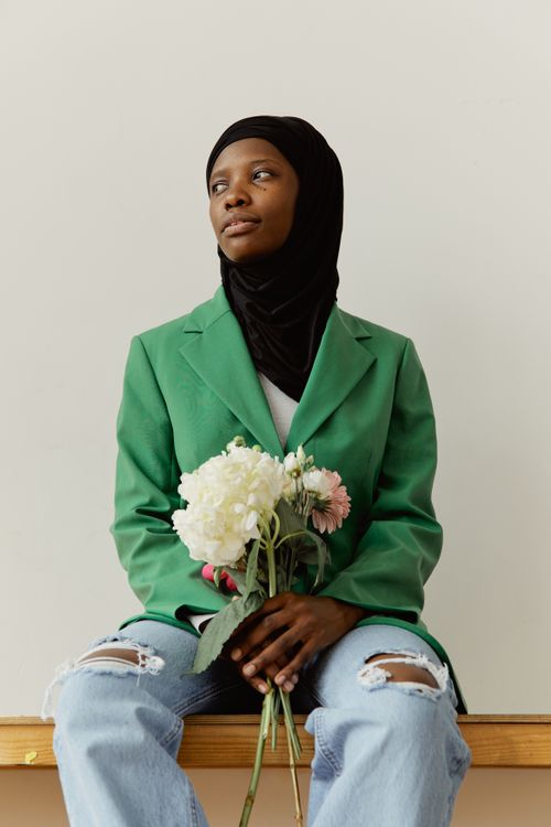 Free Portrait of a woman in a green blazer and hijab holding flowers indoors. Stock Photo