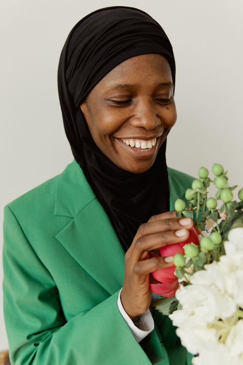 Free Smiling woman in a green blazer gently holding a bouquet of flowers. Stock Photo