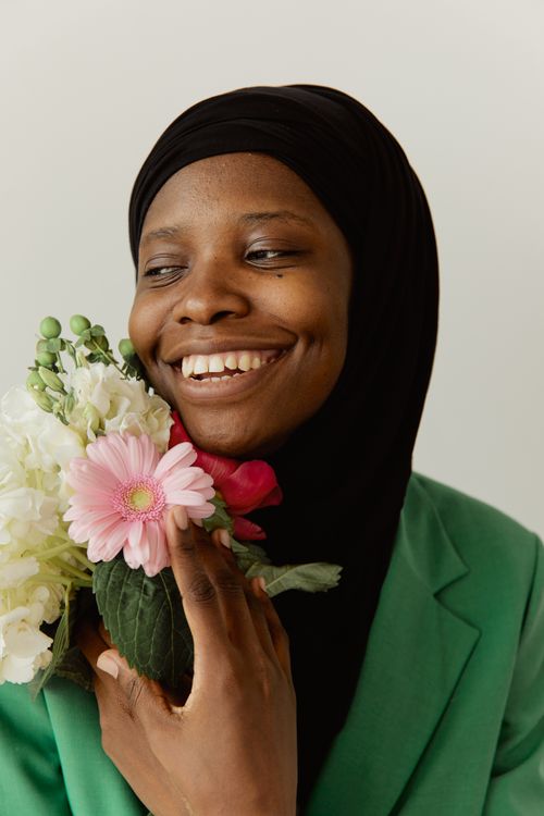 Free Smiling black woman in a minimalist setting holding vibrant flowers, conveying happiness. Stock Photo