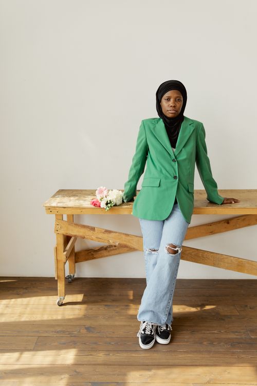Free Stylish woman in green blazer and hijab poses indoors with a bouquet on a wooden table. Stock Photo