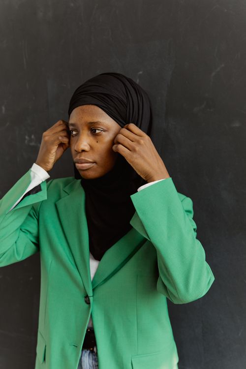 Free A thoughtful woman wearing a green blazer and black hijab against a dark background. Stock Photo