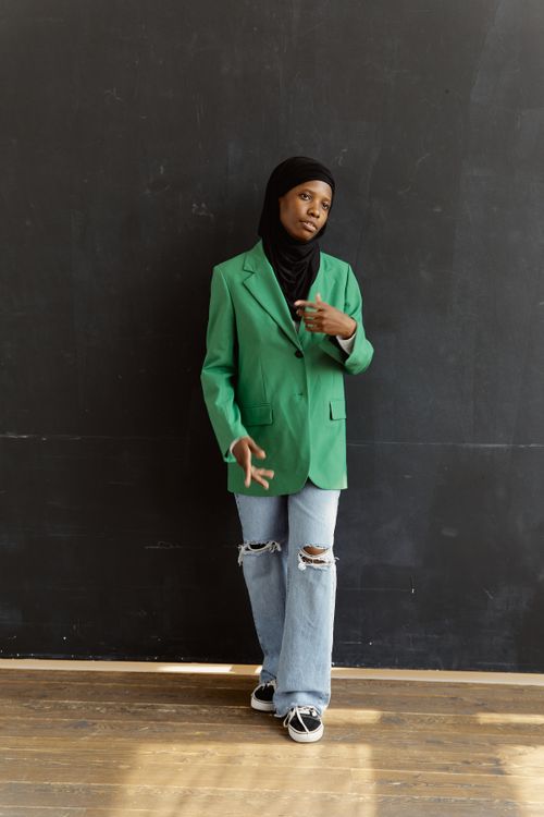 Free Stylish portrait of a black woman in a green blazer and hijab, standing confidently against a dark background. Stock Photo