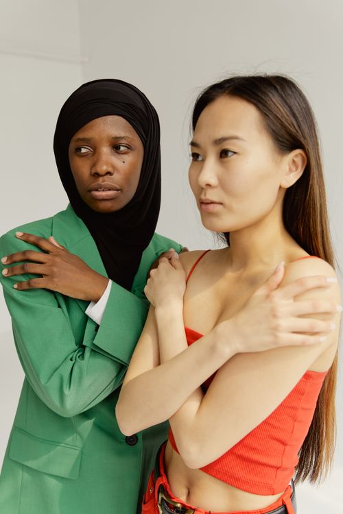 Free Studio portrait of two women, one in hijab and one in sleeveless top, embracing togetherness. Stock Photo