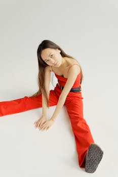 Stylish Asian woman in a red outfit posing creatively against a white background.