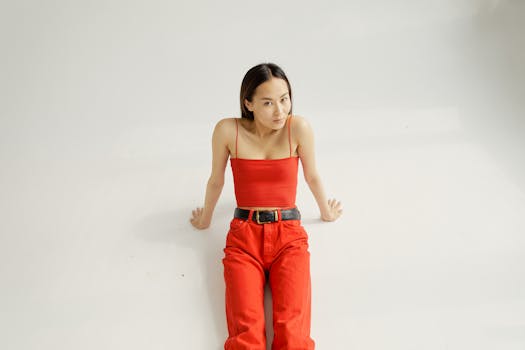 Asian woman in red sitting in studio, wearing spaghetti strap top and relaxed posture.