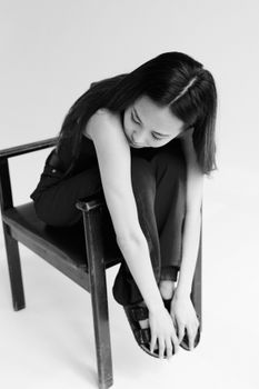 Black and white studio portrait of a woman seated on a wooden chair, creating a timeless and artistic aesthetic.