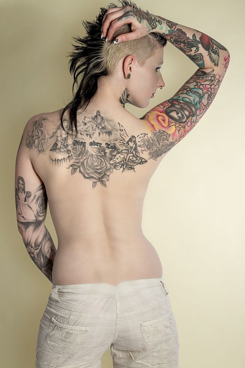 Free Back view of a tattooed woman with a mohawk, showcasing body art in a studio setting. Stock Photo