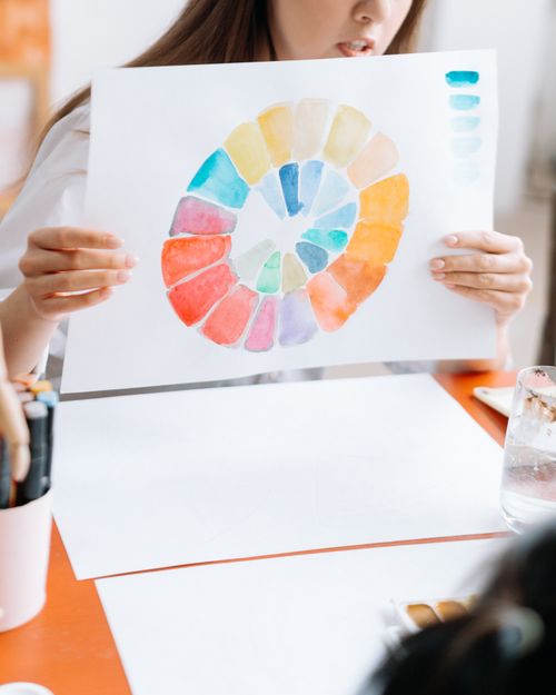 Free Hands holding a watercolor circle showcasing a full color palette during an art workshop setting indoors. Stock Photo