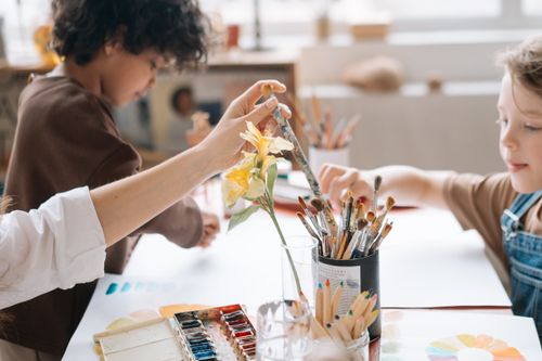 Free Children painting and drawing together in an art workshop, holding paintbrush and using colors. Stock Photo